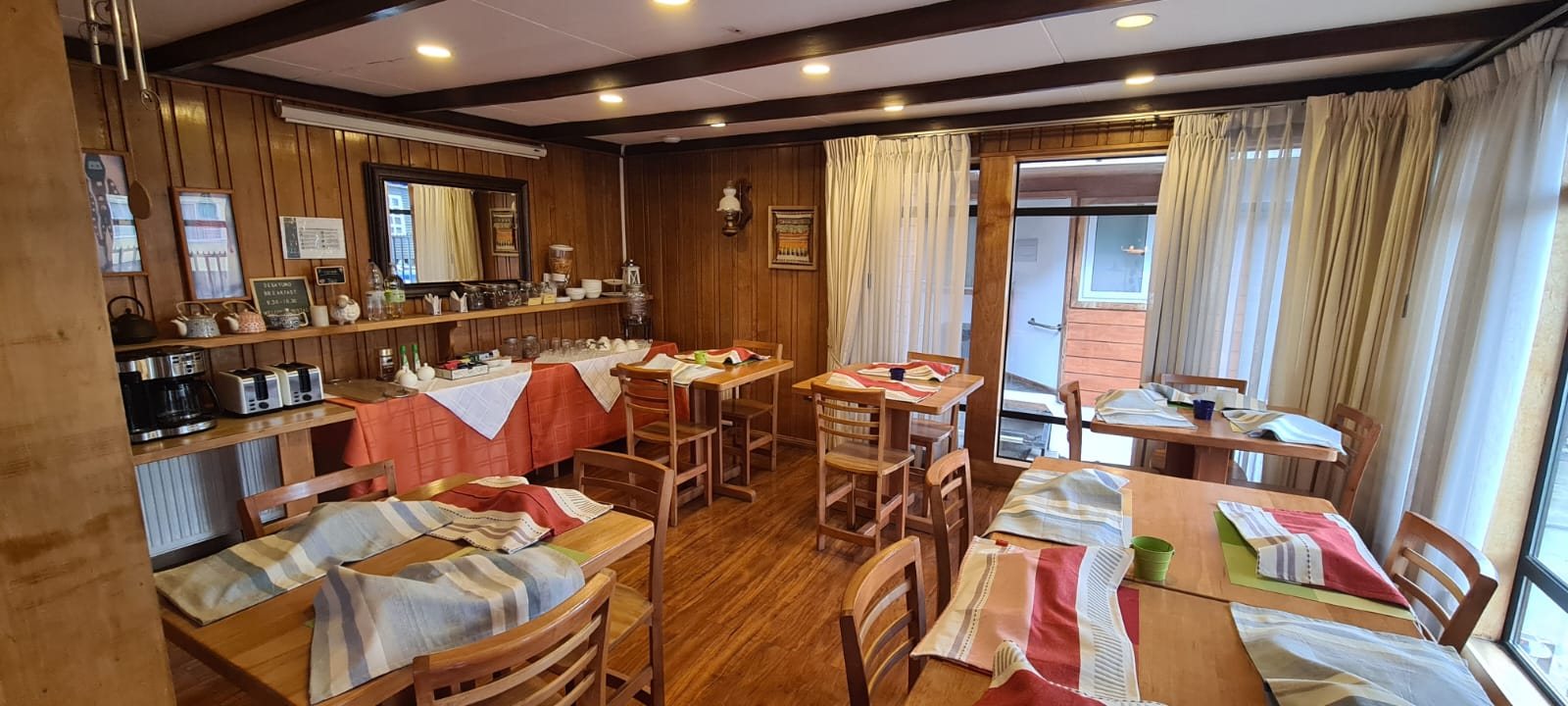 Sala del desayuno con mesas de madera, manteles y el mesón del desayuno